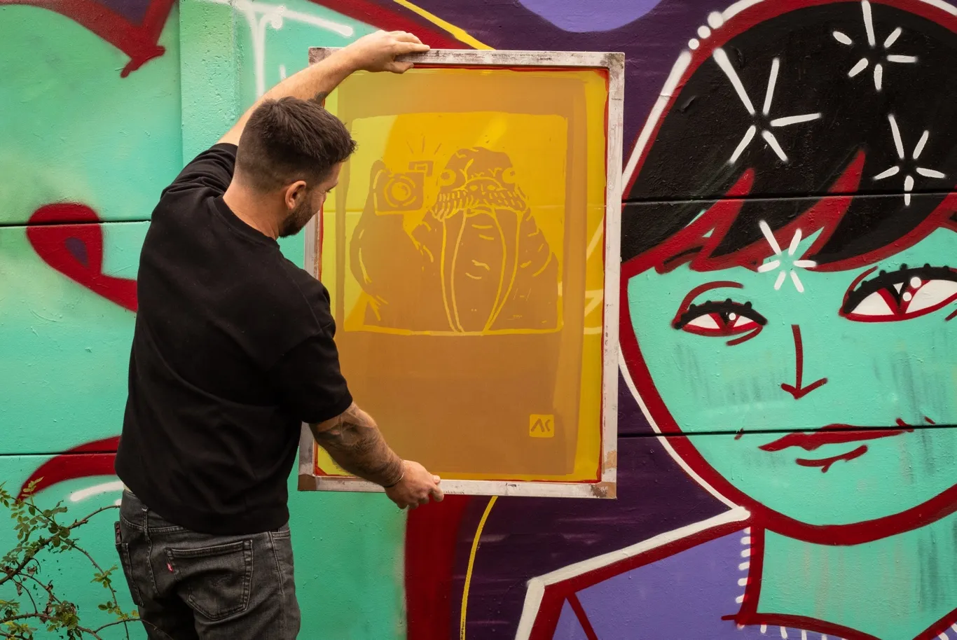 Atelier sérigraphie lors d'un AKDay : un membre de l'équipe lève un écran imprimé devant une fresque murale