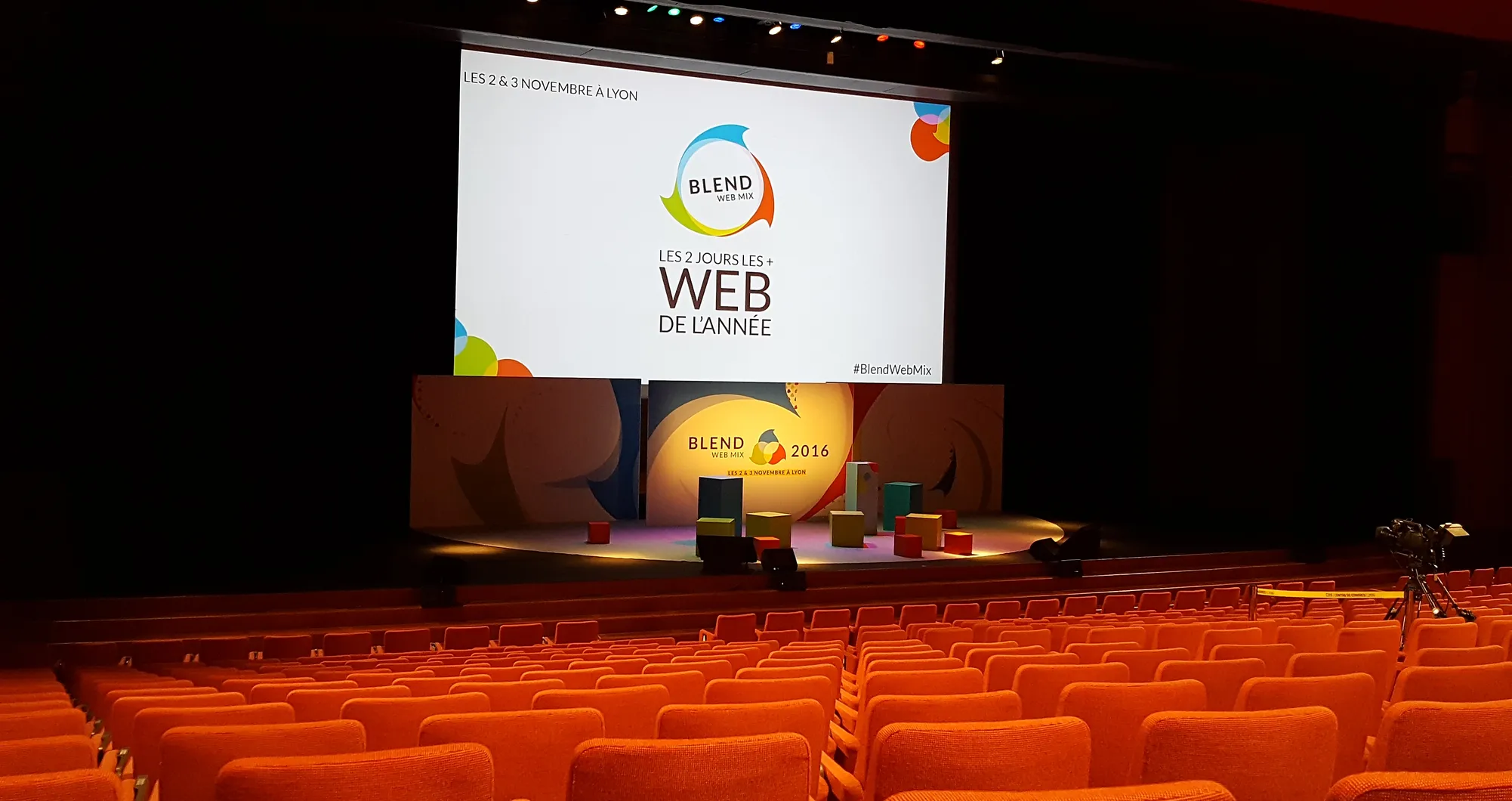 Auditorium aux fauteuils orange face à une scène affichant « WEB DE L'ANNÉE »