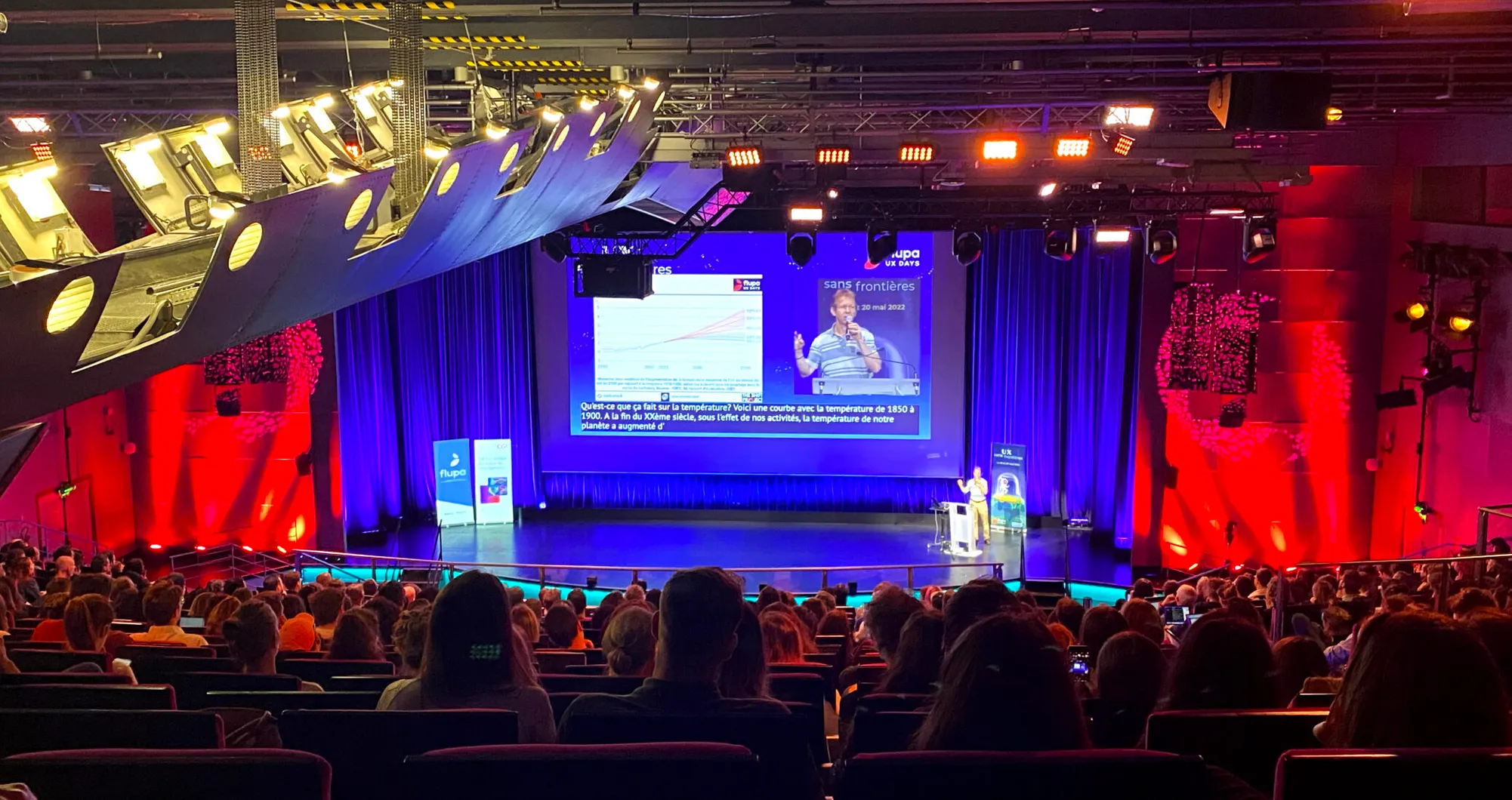 Auditorium rempli face à une scène éclairée en rouge et bleu