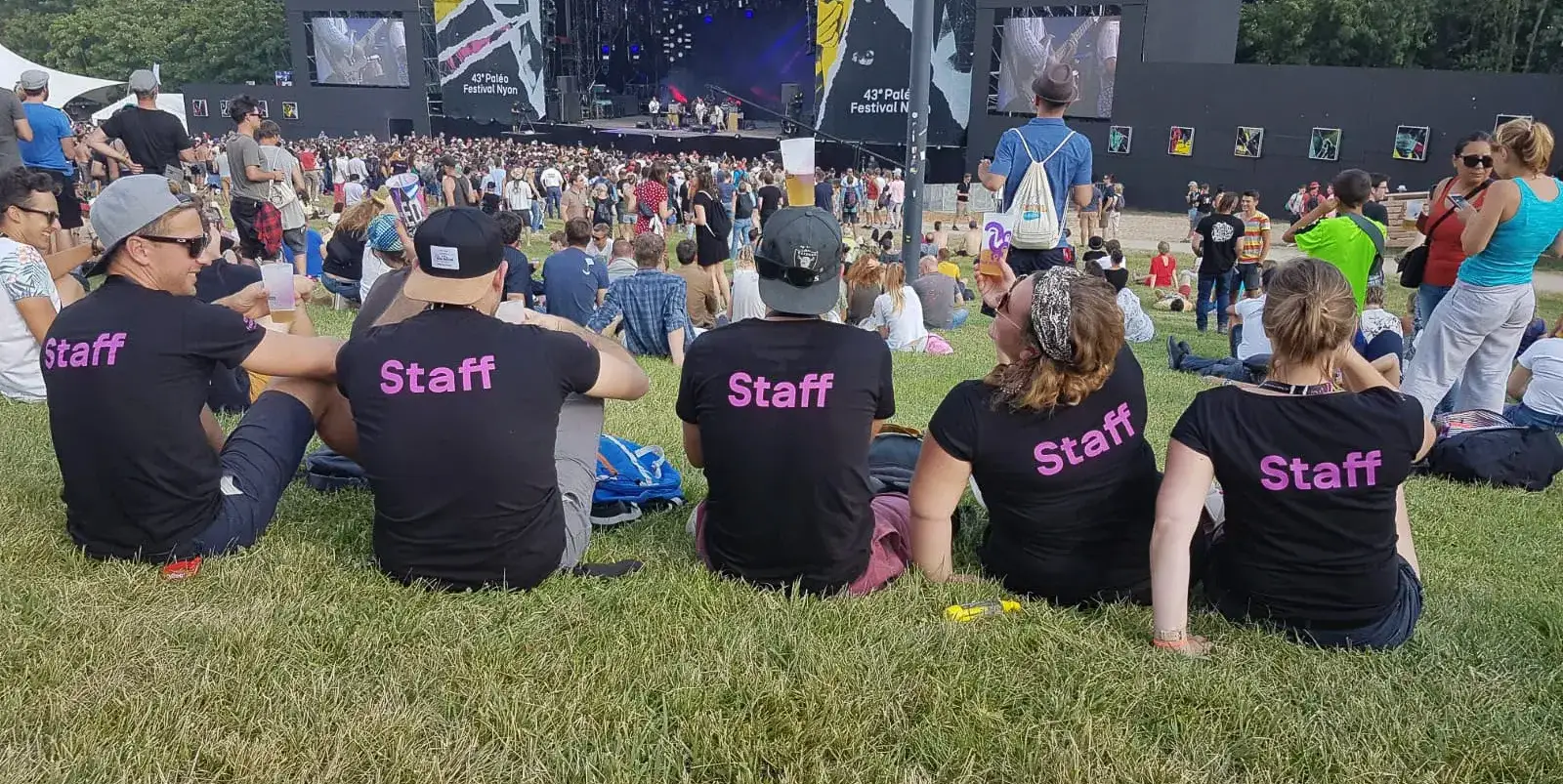 Staff volunteers in black t-shirts resting on the grass near a stage