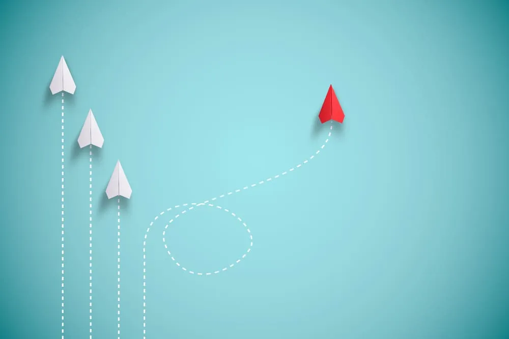 Change management: 3 white paper planes heading in the same direction and a red plane going off in another path