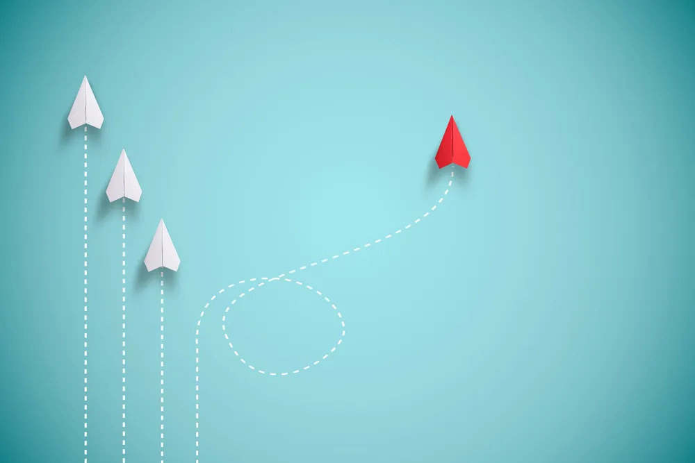 Change management: 3 white paper planes heading in the same direction and a red plane going off in another path