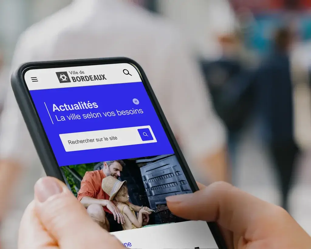 Close-up of the top of the new City of Bordeaux website homepage on a mobile phone held by a resident in the city's streets