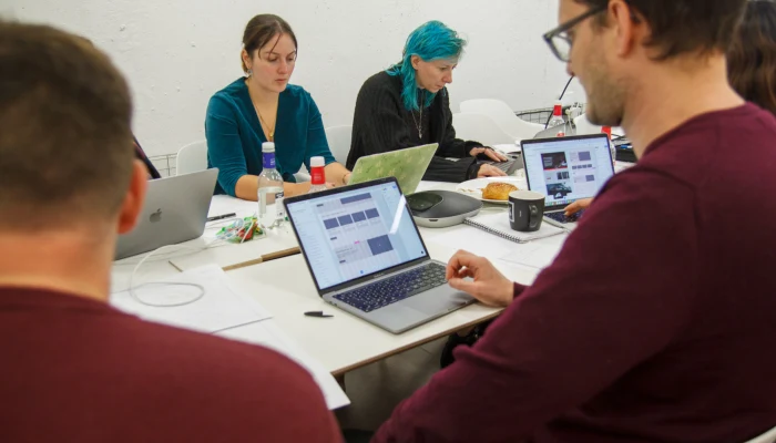 Design workshop around a table, laptops showing wireframes