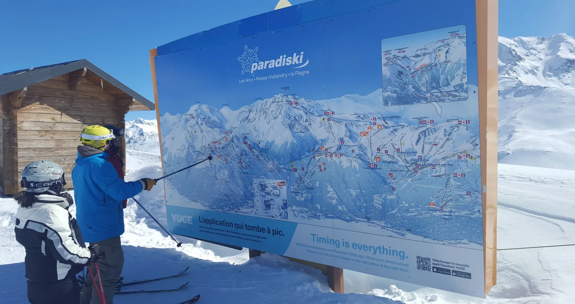 Deux skieurs consultent un grand plan des pistes enneigées « paradiski »