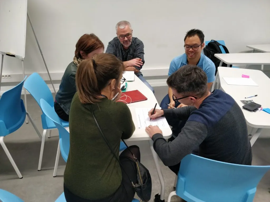Group of people around a table, writing, deep in thought - UXcamp 2018