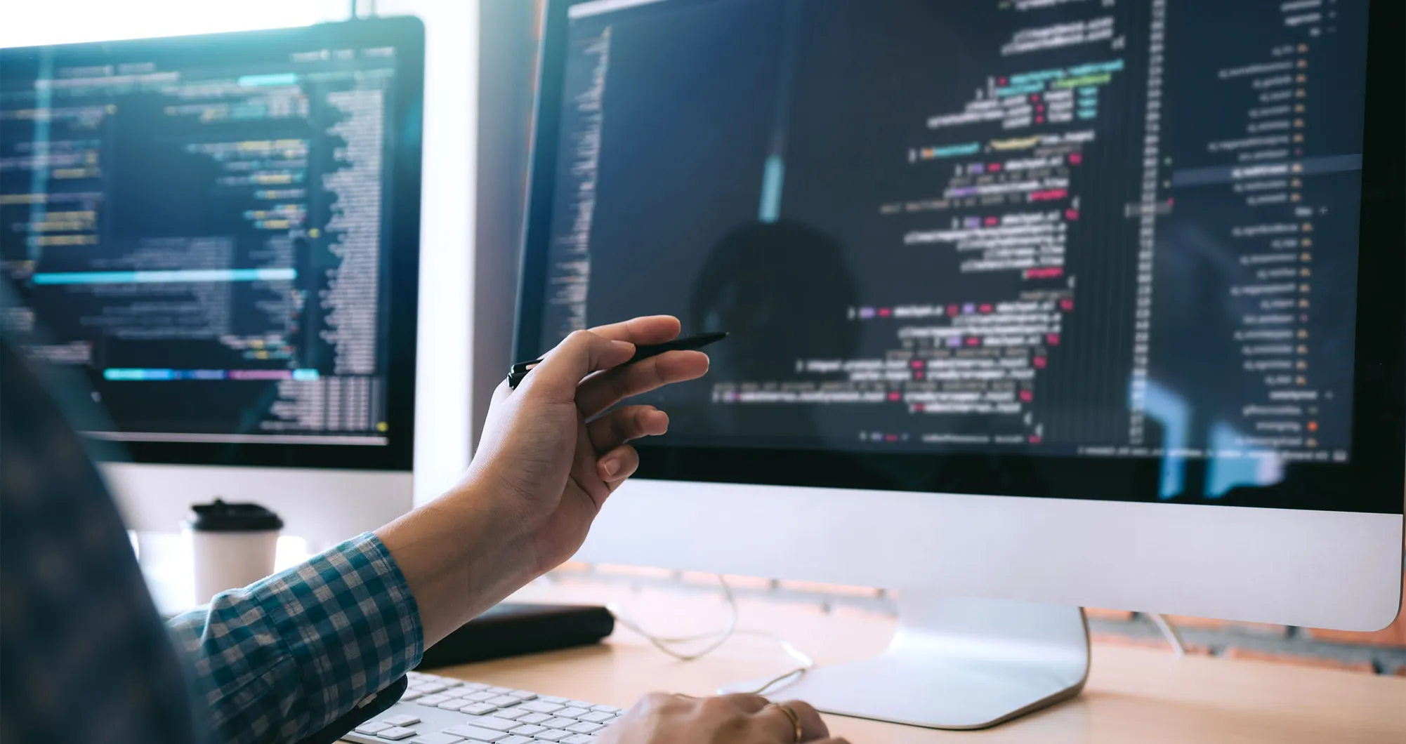 Hand pointing at code displayed across two computer monitors