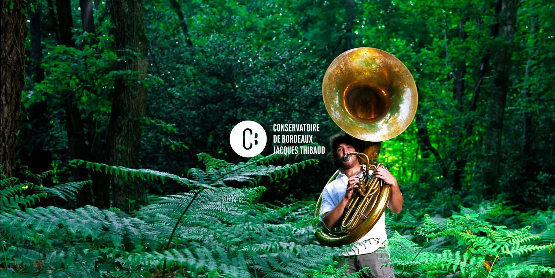 Musicien portant un soubassophone dans une forêt, avec le logo du Conservatoire de Bordeaux