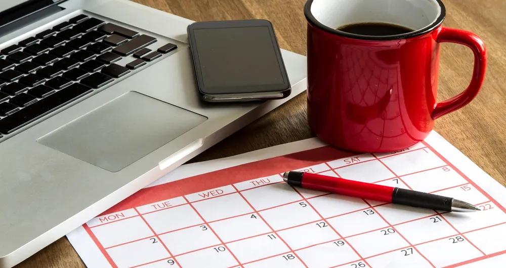 Ordinateur portable, téléphone, tasse rouge et calendrier avec stylo sur une table