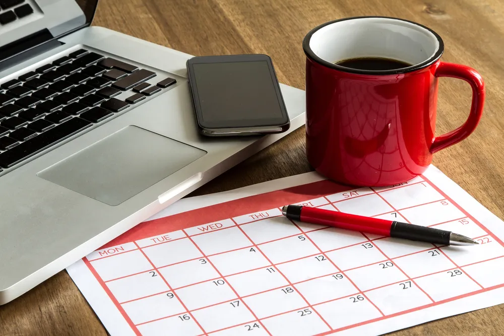 Ordinateur portable, téléphone, tasse rouge et calendrier avec stylo sur une table