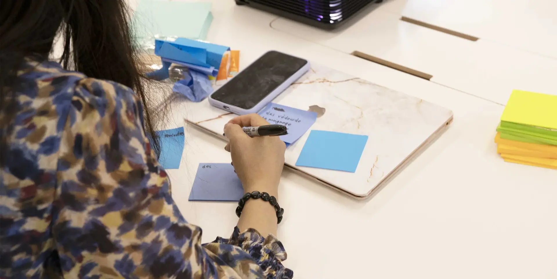 Participante écrivant sur un post-it posé sur un ordinateur portable fermé pendant un atelier