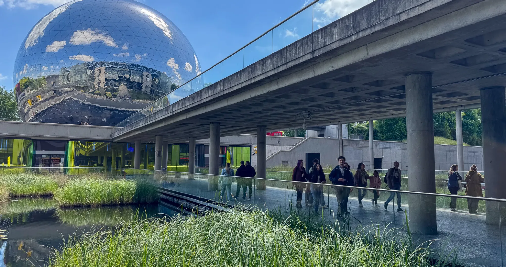 Passerelle sous une structure en béton devant un grand globe réfléchissant