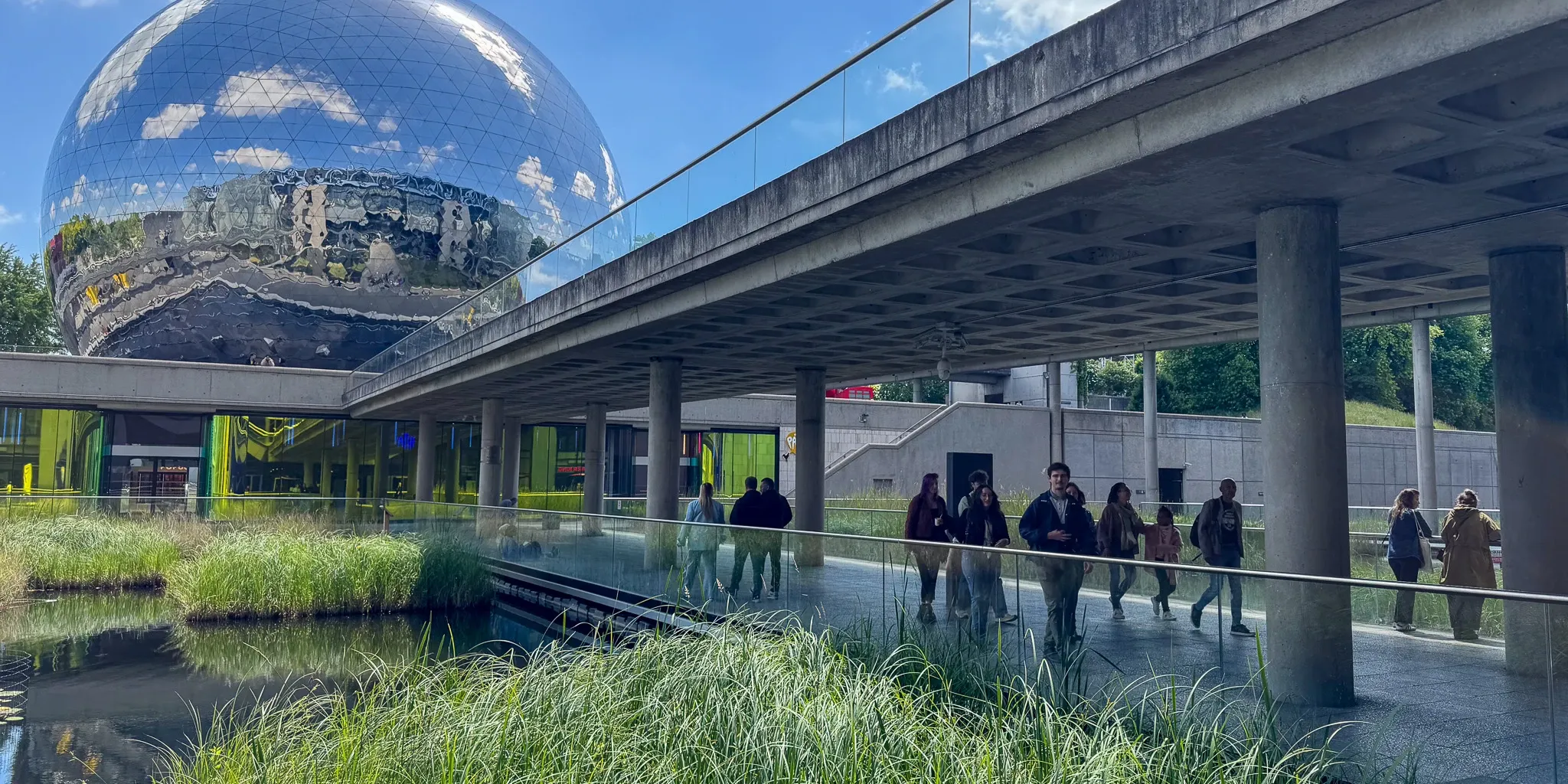Passerelle sous une structure en béton devant un grand globe réfléchissant