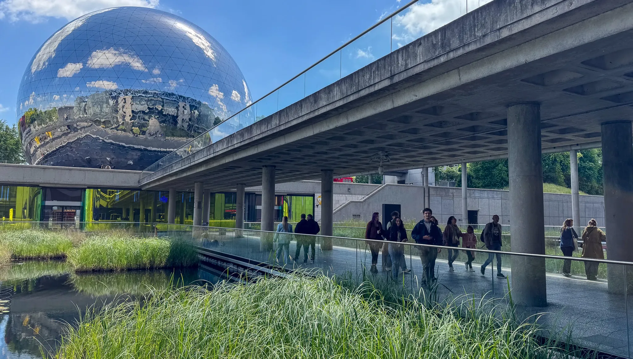 Walkway beneath a concrete structure in front of a large reflective globe