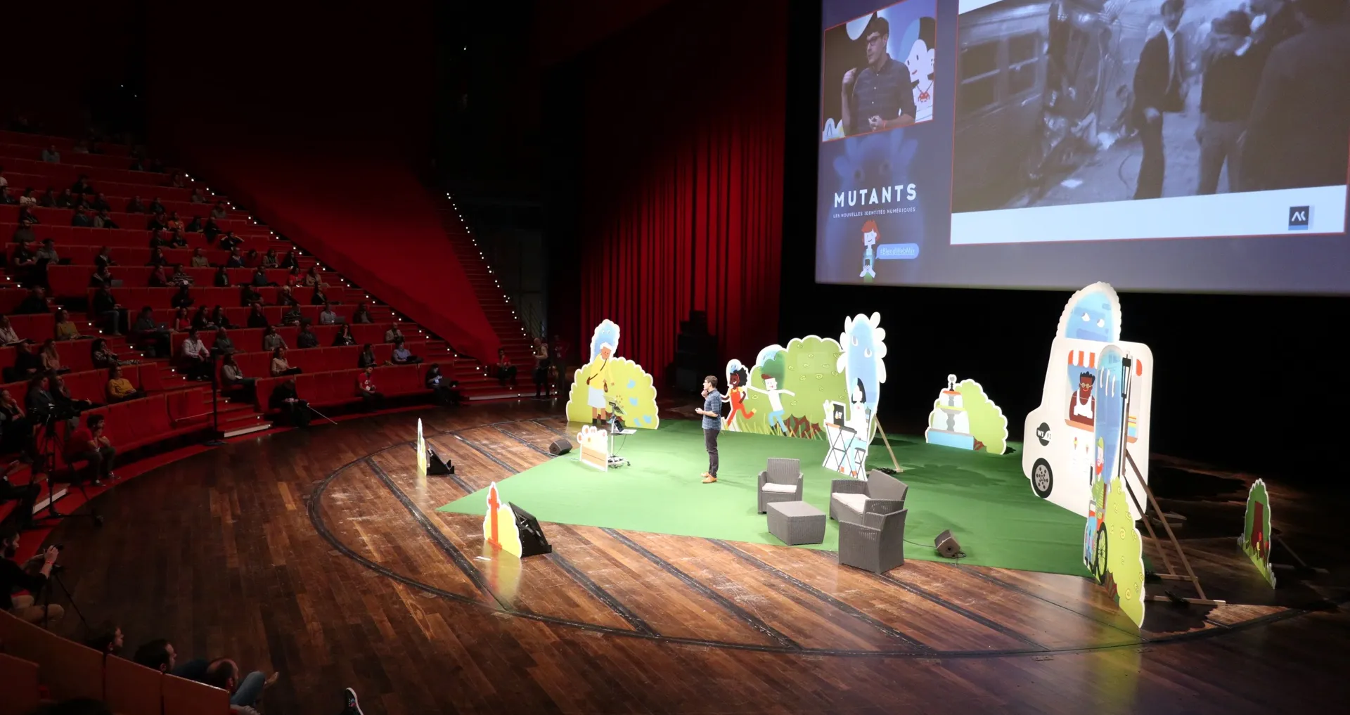 Scène d'auditorium avec silhouettes en carton, écran « MUTANTS » et public dans les gradins