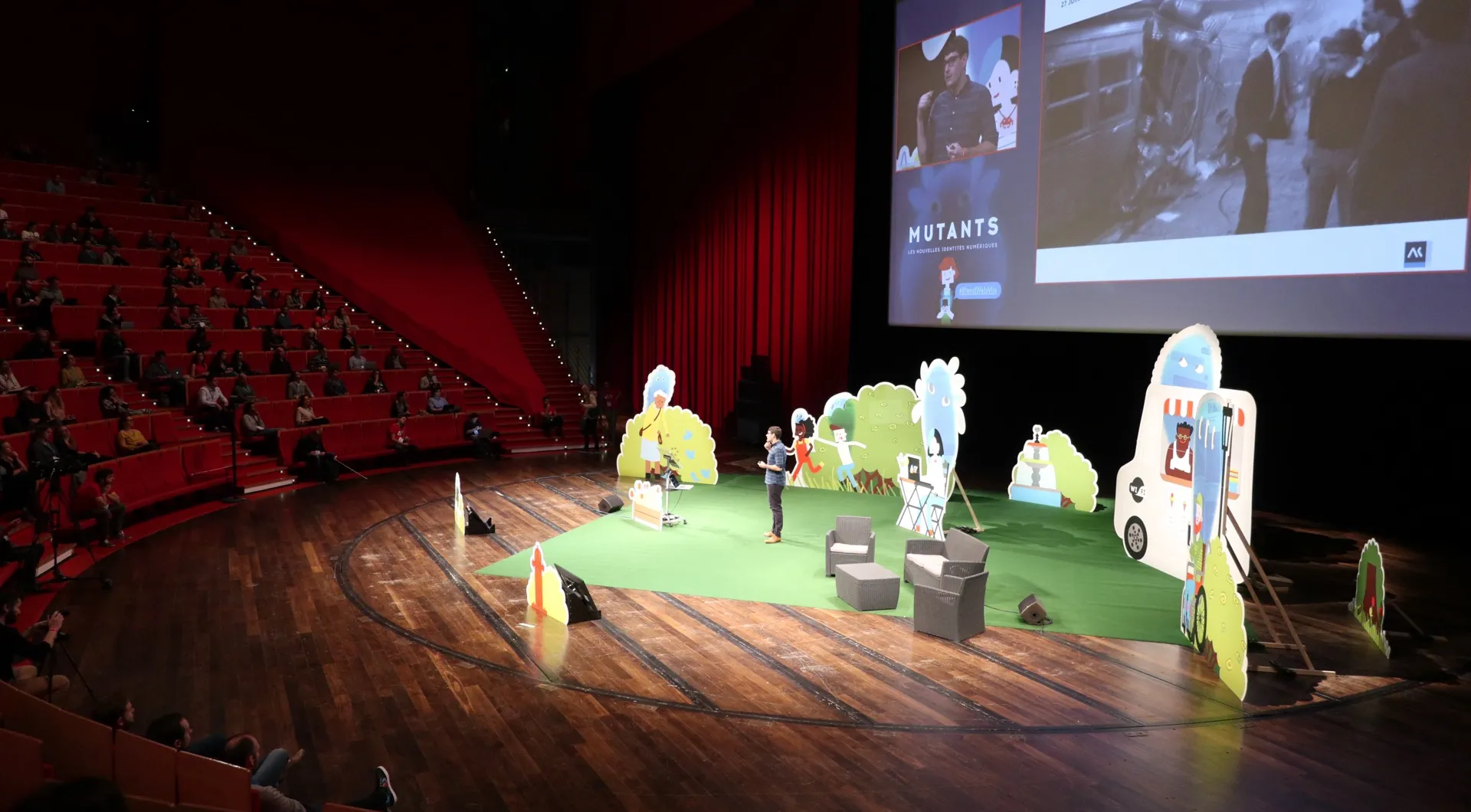 Scène d'auditorium avec silhouettes en carton, écran « MUTANTS » et public dans les gradins