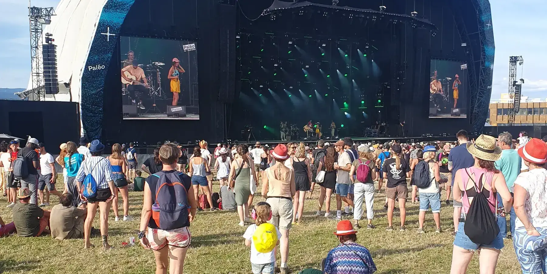 Véga stage in profile with festival-goers on the grass in the sun