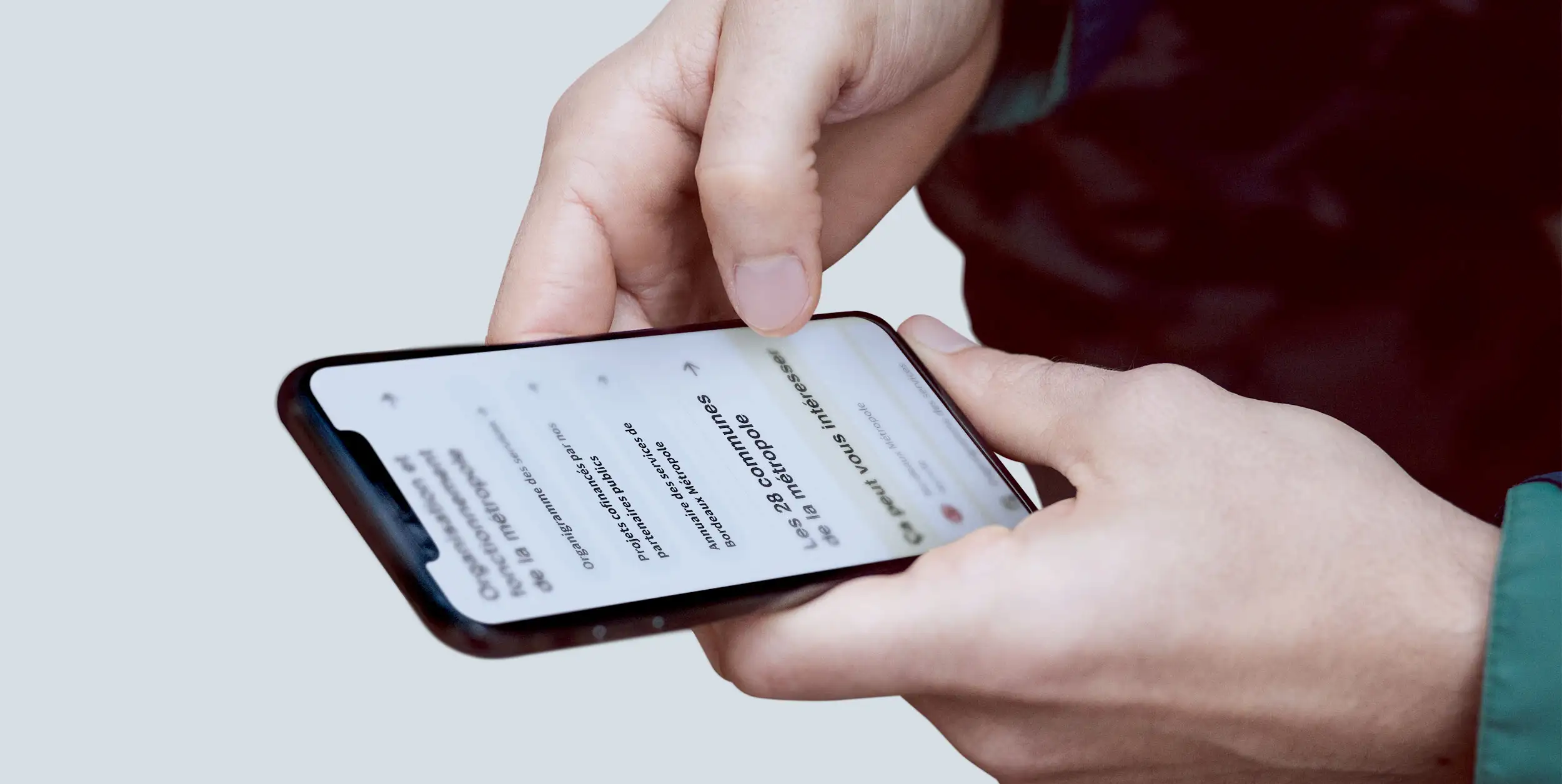 Smartphone tenu en main affichant la page carrefour en version mobile, avec l’entrée « Les 28 communes de la métropole »