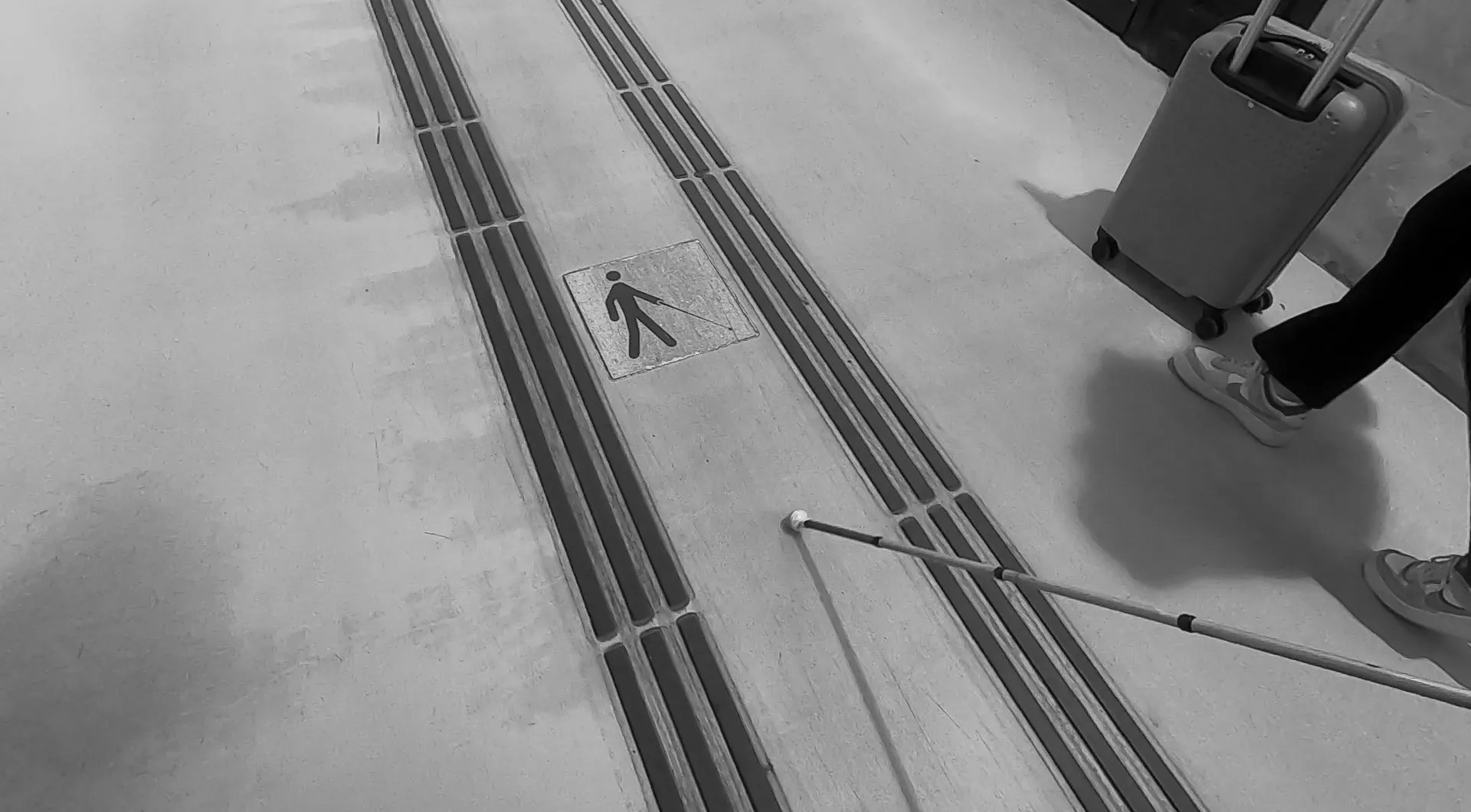 Floor with tactile strips, pedestrian symbol, white cane, and suitcase