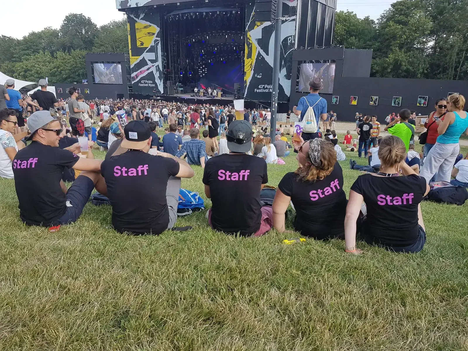 Staff volunteers in black t-shirts resting on the grass near a stage