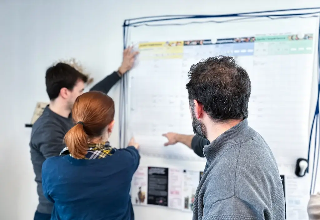Three members of a working group in deep discussion around a large sheet, sharing ideas during a meeting