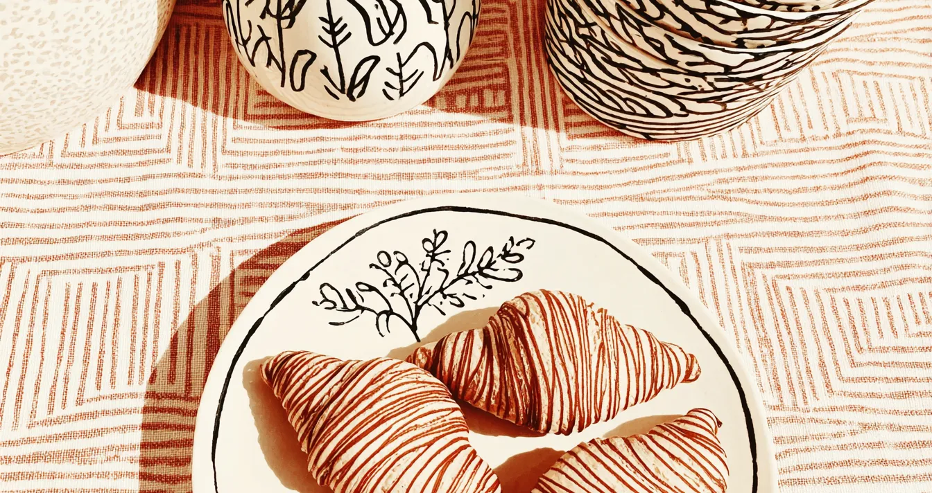 Trois croissants décorés de lignes rouges sur une assiette assortie à la vaisselle