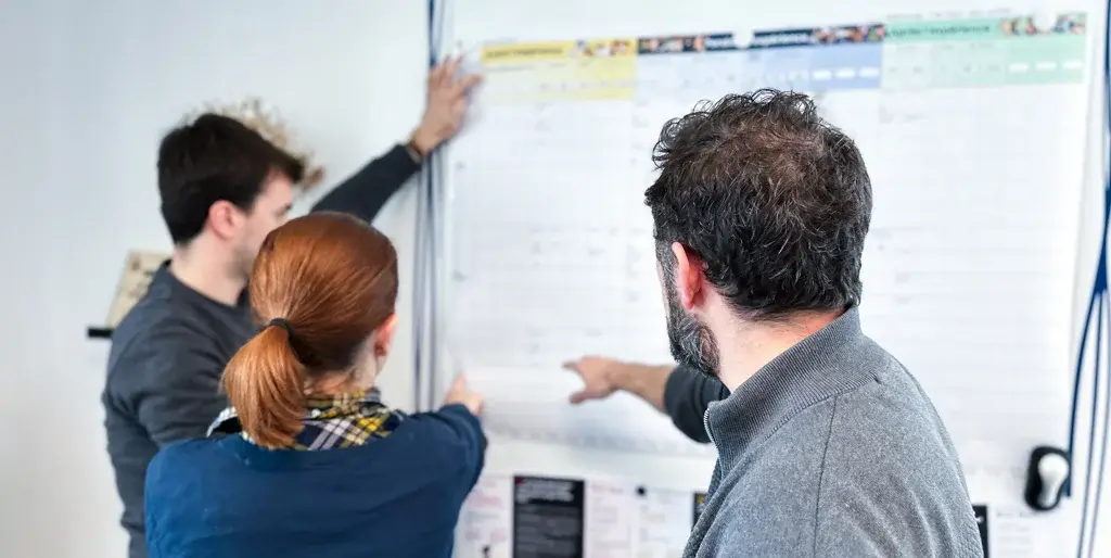 Trois membres d’un groupe de travail en pleine discussion autour d’une feuille grand format, échangeant des idées lors d’une réunion