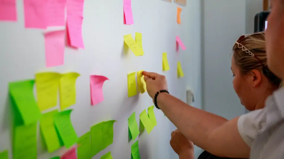 Two people in a workshop placing sticky notes on the wall