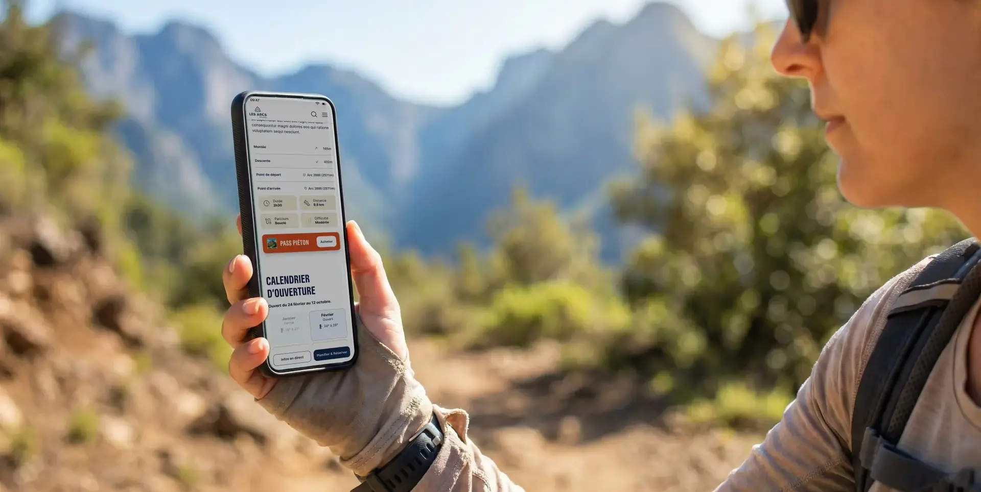 A person holds a smartphone displaying a hiking app with a 'Pedestrian Pass' button and an opening calendar, against a backdrop of sunny mountains.