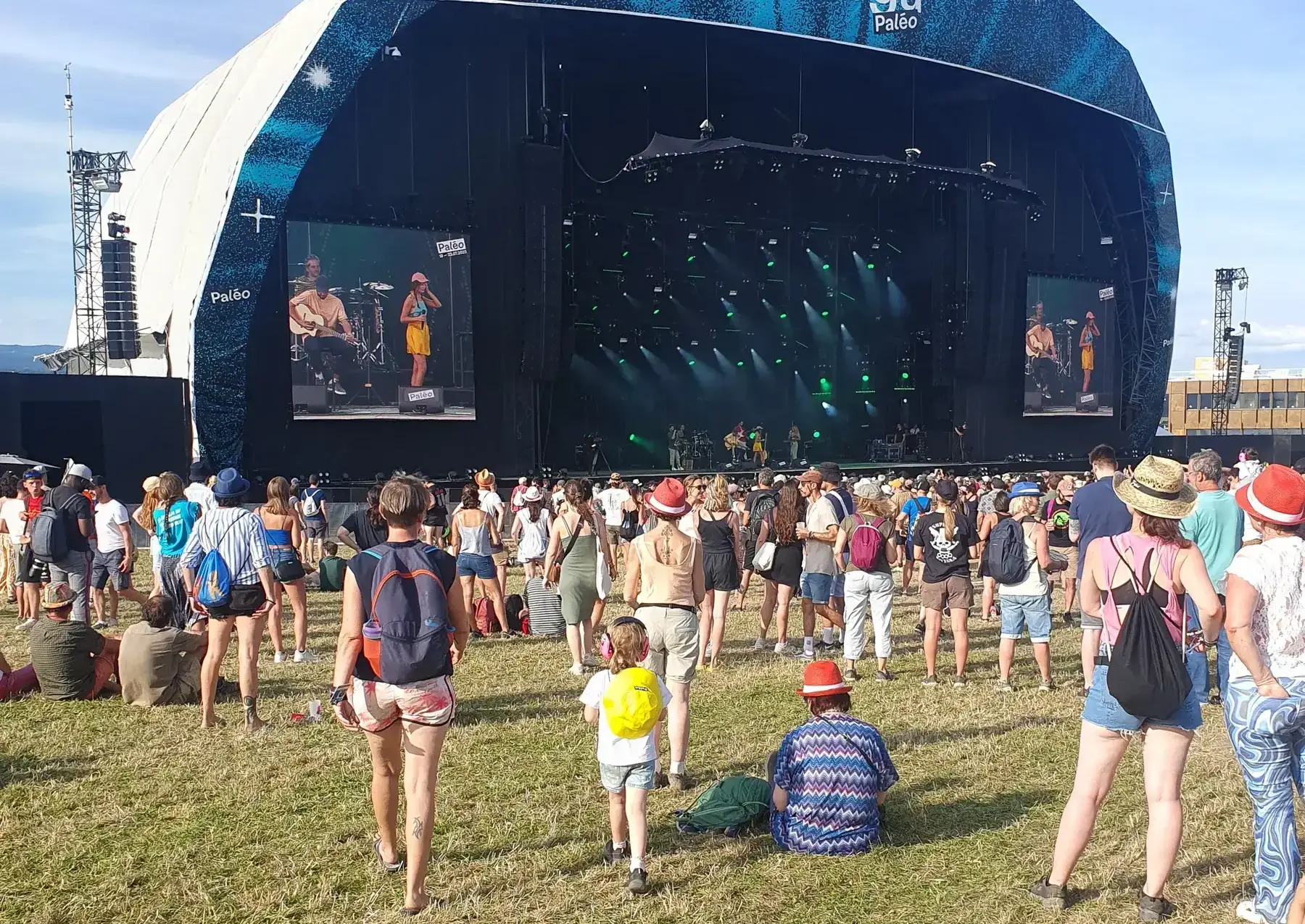 Véga stage in profile with festival-goers on the grass in the sun