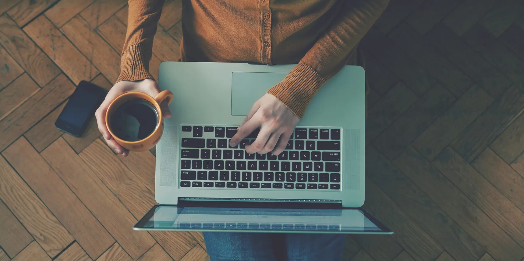 Overhead view of a person holding a mug while using a laptop