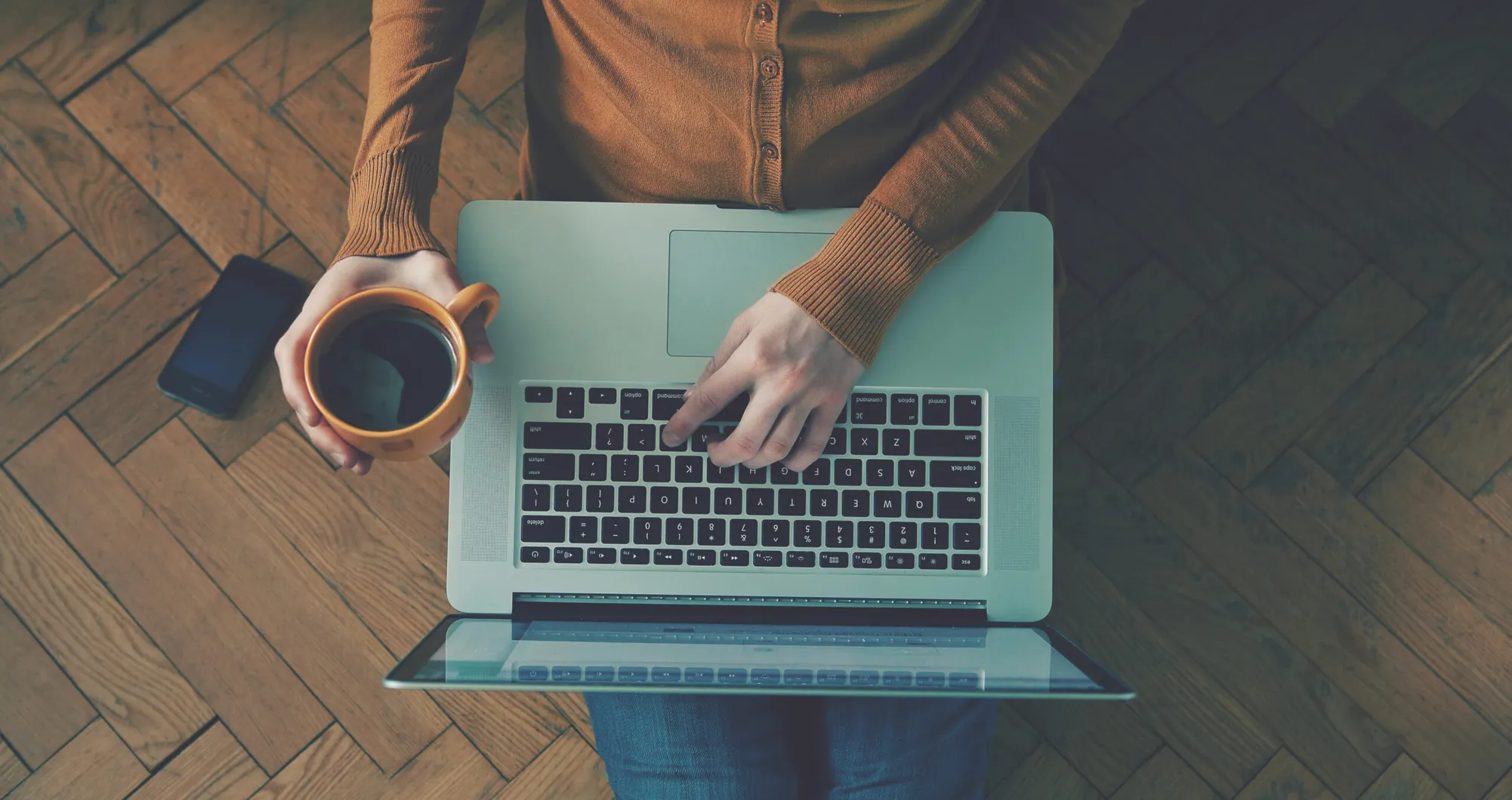 Vue de dessus d'une personne tenant une tasse tout en utilisant un ordinateur portable