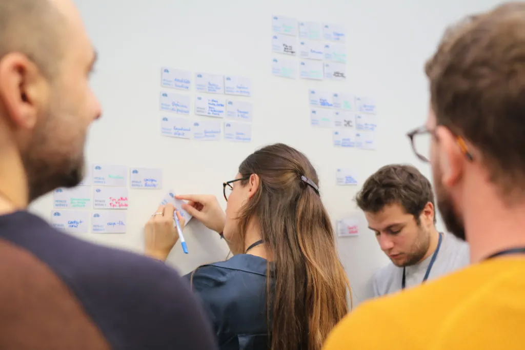 Woman seen from behind writing on a sticky note on the wall - UXcamp 2018
