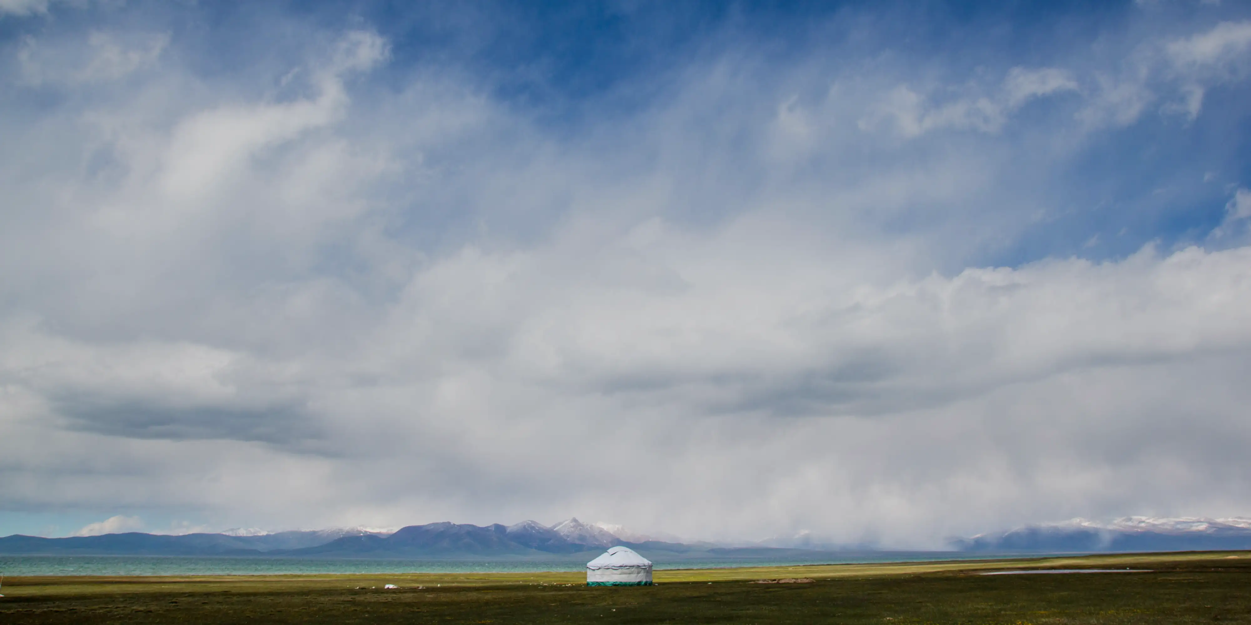 Yourte blanche dans une plaine au pied de montagnes, sous un grand ciel nuageux, photographiée par un membre de l’équipe.