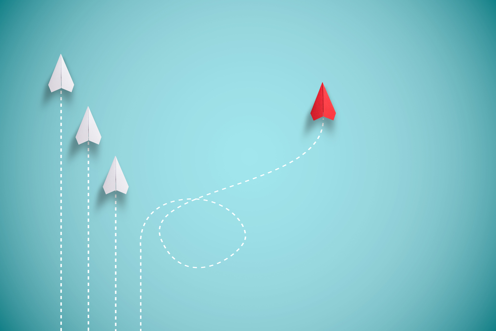 Conduite de changement : 3 avions en papier blancs dans la même direction et un avion rouge qui part dans un autre chemin