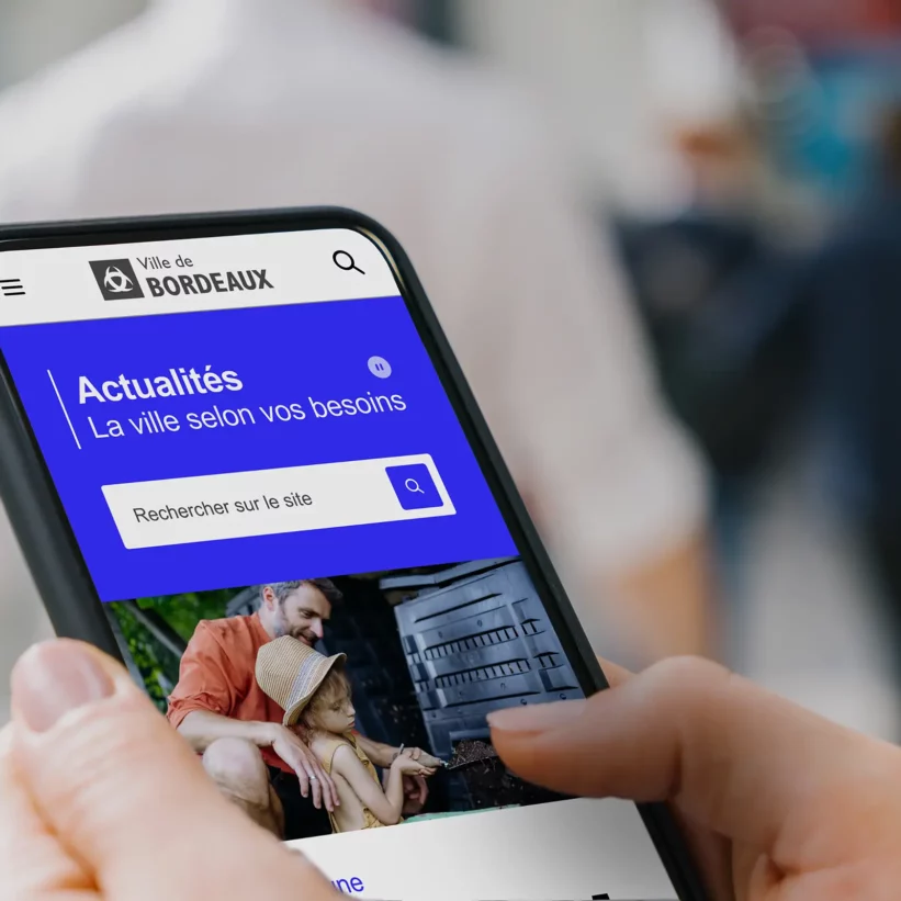 Zoom sur le haut de la page d'accueil du nouveau site de la ville de Bordeaux sur un écran de téléphone portable tenu par un cityon dans les rues de la ville